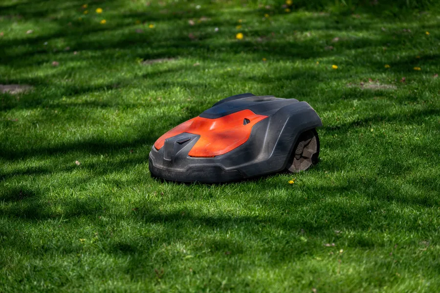 Robottiruohonleikkuri leikkaa nurmikkoa kauniissa puutarhassa, ympärillä vihreää ruohoa ja auringonvalo.